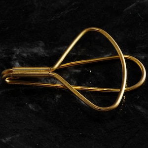 May include: A gold-colored metal eye lash curler with a curved design.