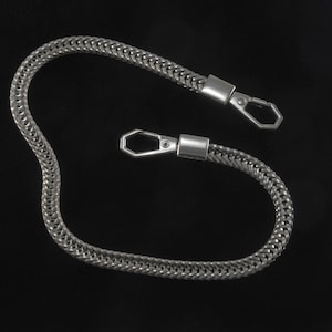 Puede incluir: Una cadena de plata con dos cierres de plata. La cadena está hecha de un patrón tejido.