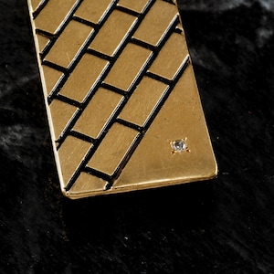 May include: A gold-toned pendant with a brick pattern and a small clear rhinestone in the center.