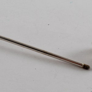 May include: A silver metal rod with a threaded end and a decorative, threaded, crown-shaped tip. The rod and tip are separated.