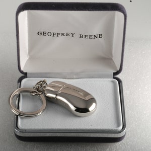May include: A silver mouse keyring in a blue velvet box with the text "GEOFFREY BEENE" on the inside of the lid.