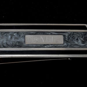 May include: A silver money clip with a black and grey marbled design. The clip has the word "ENL" engraved on the front.