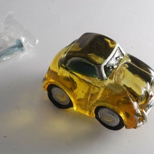 May include: A yellow glass car shaped cabinet knob with a silver trim. The knob comes with a silver screw.