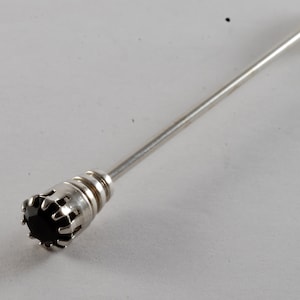 May include: A silver tie tack with a black gemstone set in a crown-like design.