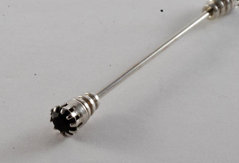 May include: A silver tie tack with a black gemstone set in a crown-like design.