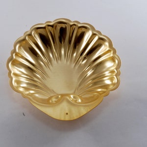 May include: A gold-colored metal shell-shaped dish. The dish has a smooth, shiny surface and a scalloped edge.