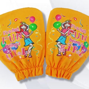 May include: Two orange fabric arm warmers with the text "It's so much FUN being a GIRL" and a cartoon illustration of a dancing girl holding balloons. The arm warmers have a gathered elastic cuff.