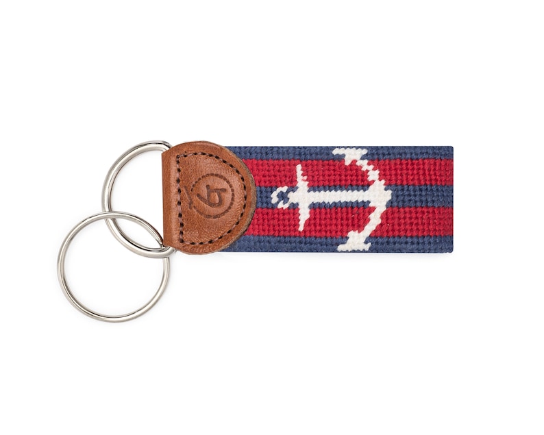 May include: A blue and red striped key chain with a white anchor design and a brown leather fob. The key chain has a double ring.