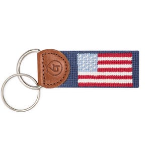 May include: A blue and white American flag keyring with a brown leather loop. The keyring has a silver double ring.