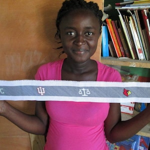 May include: A person is holding a grey and white fabric strip with the text "RTC" and a stylised "Psi" symbol, along with a scale, a red cardinal, and a basketball.