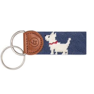 May include: A navy blue key chain with a white dog with a red collar and a brown leather fob with a logo.
