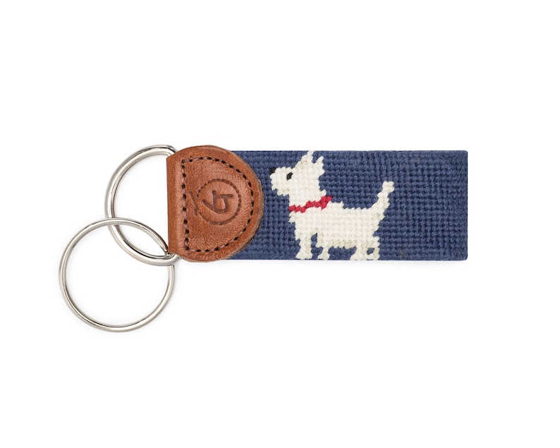 May include: A navy blue key chain with a white dog with a red collar and a brown leather fob with a logo.