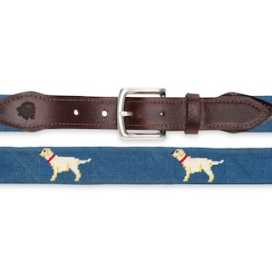 May include: A blue and brown woven belt with a silver buckle. The belt features a repeated pattern of white Labrador Retrievers.
