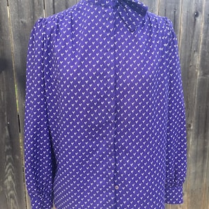 May include: A purple long-sleeved blouse with a white bird print and a high collar. The collar has a bow tie detail.