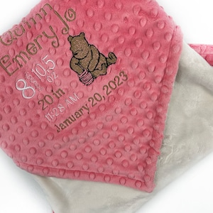 May include: A pink and white baby blanket with a Winnie the Pooh bear design. The blanket is embroidered with the text "Welcome Emery Jo", "8 lbs 10 oz", "20 in", "11:28 AM", and "January 20, 2023".