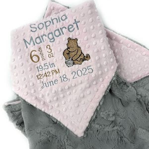 May include: A baby blanket with a pink top layer featuring the name "Sophia Margaret", weight 6 pounds 3 ounces, length 19.5 inches, time 12:42 PM, and date June 18, 2025. The blanket has a Winnie the Pooh bear design and a gray bottom layer.