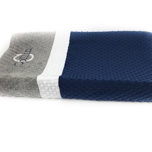 May include: A changing pad with a gray, white, and navy blue color block design. The gray section has the name "Collin" embroidered in a cursive font. The pad has a textured, dotted surface.