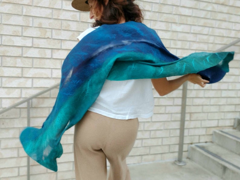 May include: A woman wearing a teal and blue ombre scarf with a white shirt and tan pants.