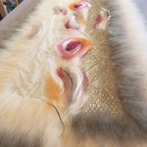 May include: A white, fluffy, felted fabric with a gold, sparkly, textured strip running down the center. The fabric is decorated with pink, orange, and white felt flowers.