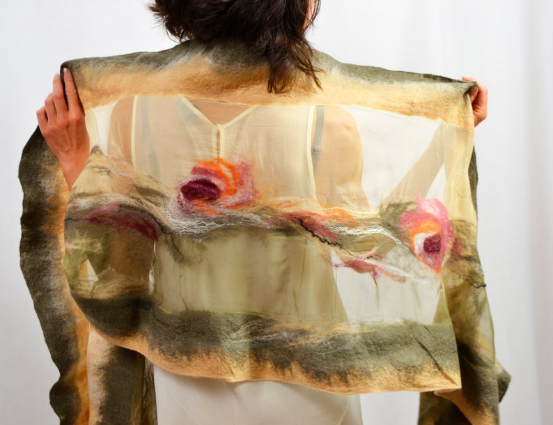 May include: A beige and green silk scarf with a floral design. The scarf has a sheer, translucent texture and features three pink, orange, and white flowers.