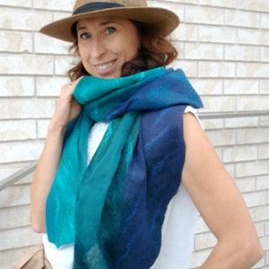 May include: A woman wearing a brown fedora hat and a blue and green gradient scarf. The scarf has a subtle pattern of white lines.