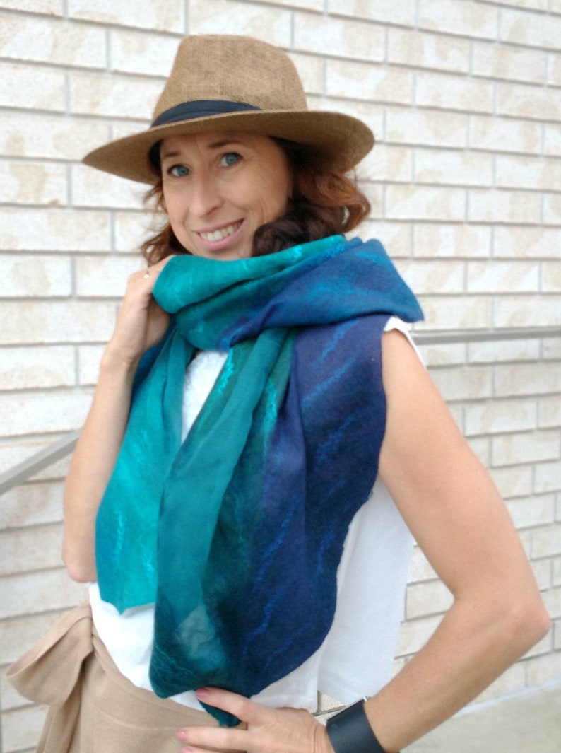 May include: A woman wearing a brown fedora hat and a blue and green gradient scarf. The scarf has a subtle pattern of white lines.