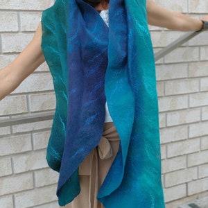 May include: A teal and blue ombre scarf with a subtle pattern. The scarf is made of a soft, flowing fabric and is worn around the neck.