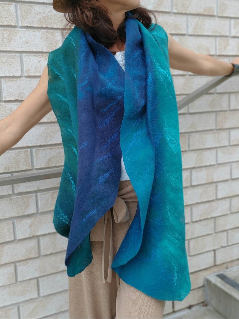 May include: A teal and blue ombre scarf with a subtle pattern. The scarf is made of a soft, flowing fabric and is worn around the neck.