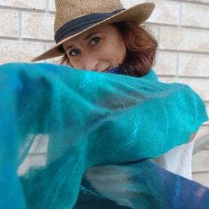 May include: A woman wearing a brown fedora and a teal blue scarf with a white background. The scarf has a subtle pattern of light blue and dark blue.