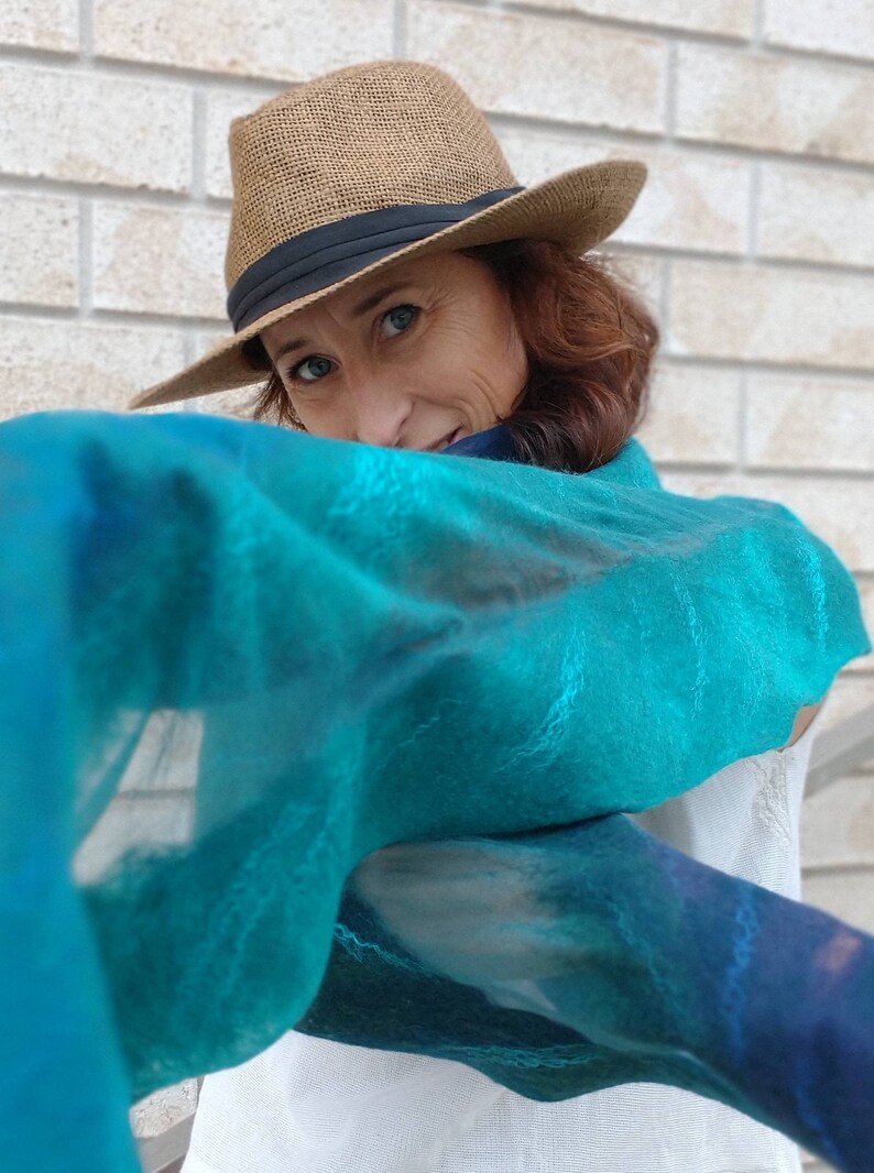 May include: A woman wearing a brown fedora and a teal blue scarf with a white background. The scarf has a subtle pattern of light blue and dark blue.