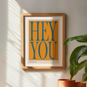 May include: A framed print with a yellow background and blue text that reads "HEY YOU" and "HAVE A NICE DAY!"
