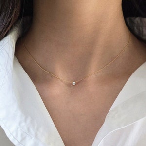 May include: A delicate gold chain necklace with a small, clear gemstone pendant.