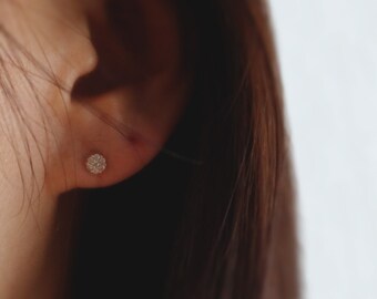 Könnte beinhalten: Nahaufnahme eines Ohrs mit einem kleinen, runden Diamant-Ohrstecker. Der Ohrring ist in Gold gefasst und hat einen Cluster aus kleinen Diamanten.