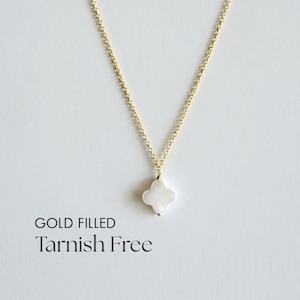 May include: A gold-filled necklace with a four-leaf clover pendant. The pendant is white and hangs from a delicate gold chain. The words "GOLD FILLED" and "Tarnish Free" are printed below the necklace.