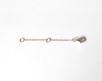 May include: A silver chain extender with a lobster clasp and two jump rings.