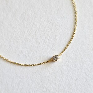 May include: A delicate gold chain necklace with a single, clear diamond pendant.