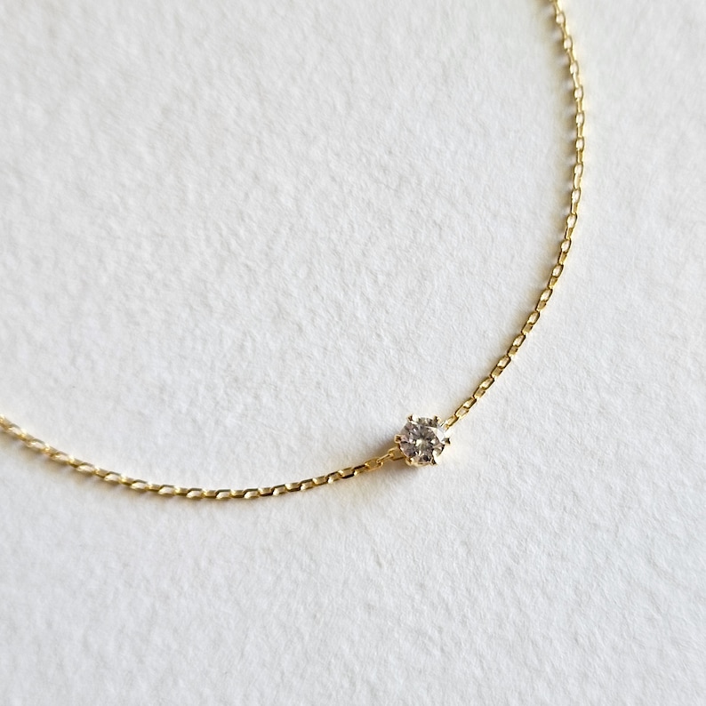 May include: A delicate gold chain necklace with a single, clear diamond pendant.