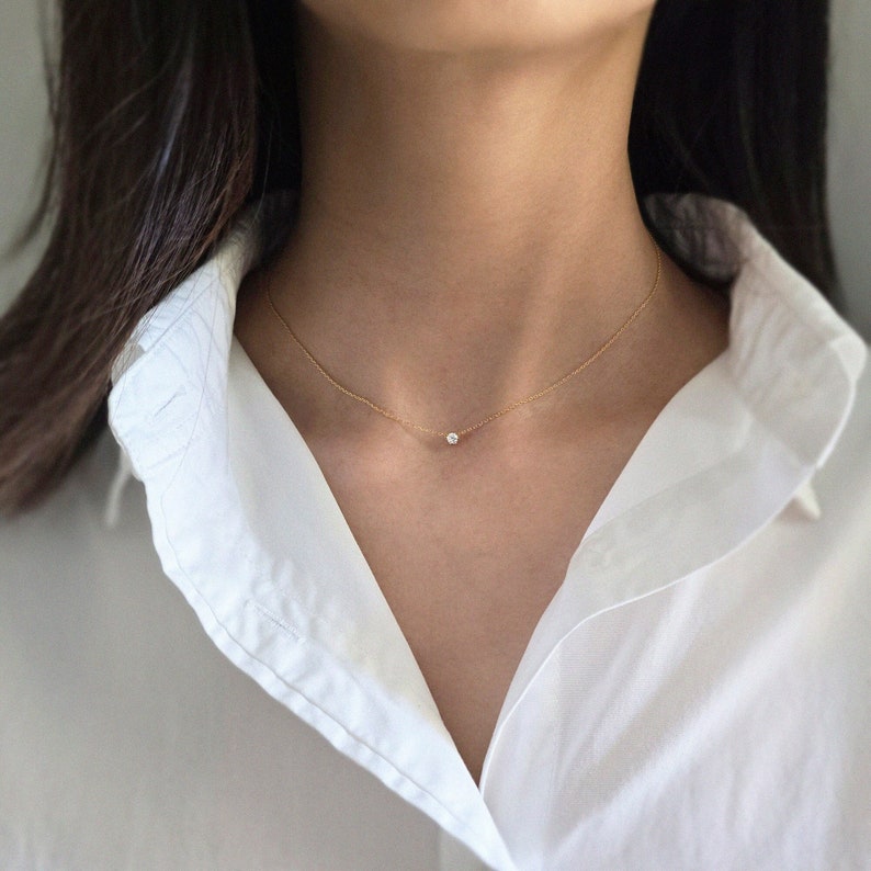 May include: A delicate gold chain necklace with a small, clear gemstone pendant.
