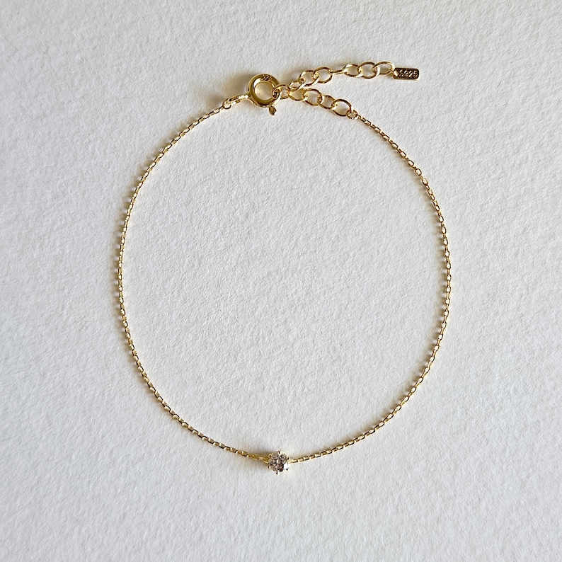 May include: A delicate gold chain bracelet with a single small clear gemstone.
