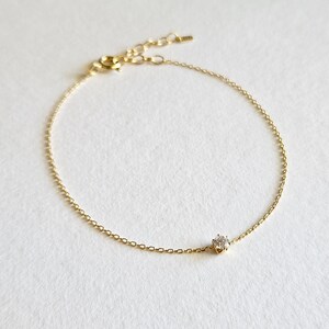 May include: A delicate gold chain bracelet with a single, clear gemstone in the center.