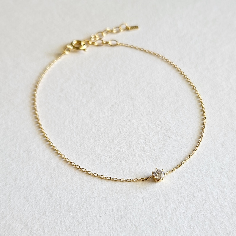 May include: A delicate gold chain bracelet with a single, clear gemstone in the center.