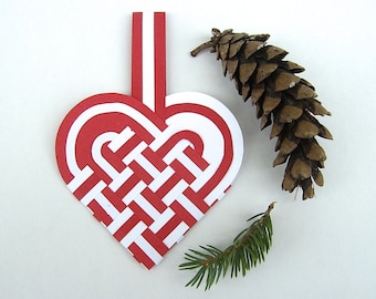 Pode incluir: Um ornamento de coração de papel vermelho e branco com um padrão tecido. O ornamento tem um cordão branco preso ao topo para pendurar.