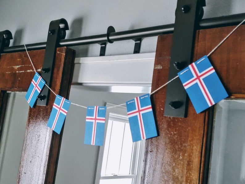 May include: A string of Icelandic flags hanging from a black metal sliding door track. The flags are blue with a white cross and red trim.
