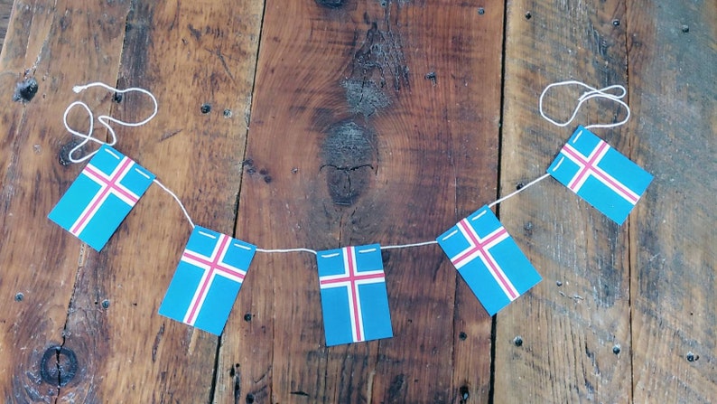 May include: A string of Icelandic flags, each featuring a blue background with a white cross and a red crossbar, hangs against a rustic wooden backdrop.