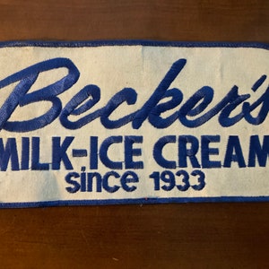 Op de afbeelding: Een witte geborduurde patch met blauwe letters die "Becker's Milk-Ice Cream since 1933" lezen.