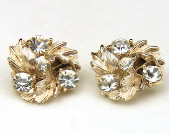 May include: A pair of gold tone earrings with clear rhinestone accents in a floral design.