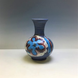 Może przedstawiać: Niebieski ceramiczny wazon z pękatym korpusem i wąską szyjką. Wazon ma kwiatowy wzór w odcieniach niebieskiego, czerwonego i białego. Wazon ma około 20 cm wysokości.