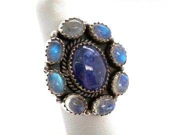 May include: A silver ring with a large blue gemstone surrounded by smaller moonstone gemstones.