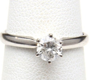 May include: A silver ring with a large, round, clear gemstone. The gemstone is set with six prongs. The ring is on a white background.