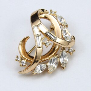 May include: A gold-toned brooch with a swirling design and clear rhinestones.